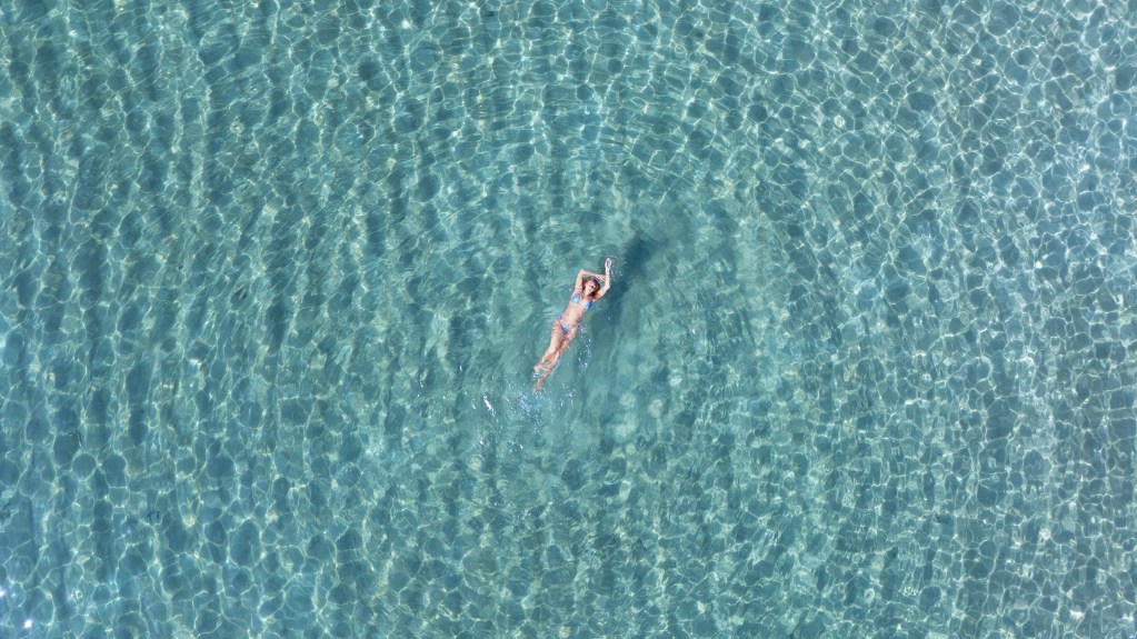 Drone aerial shot of pregnant woman floating in crystal clear turquoise ocean water for mermaid maternity