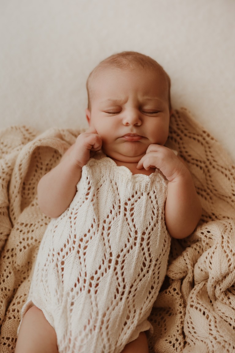 Sleeping newborn closeup with fists by chin in white knit romper