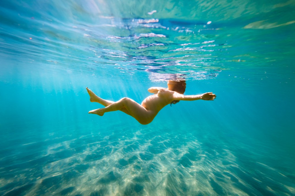 Pregnant woman reaching forward into ocean with sun rays overhead underwater photography